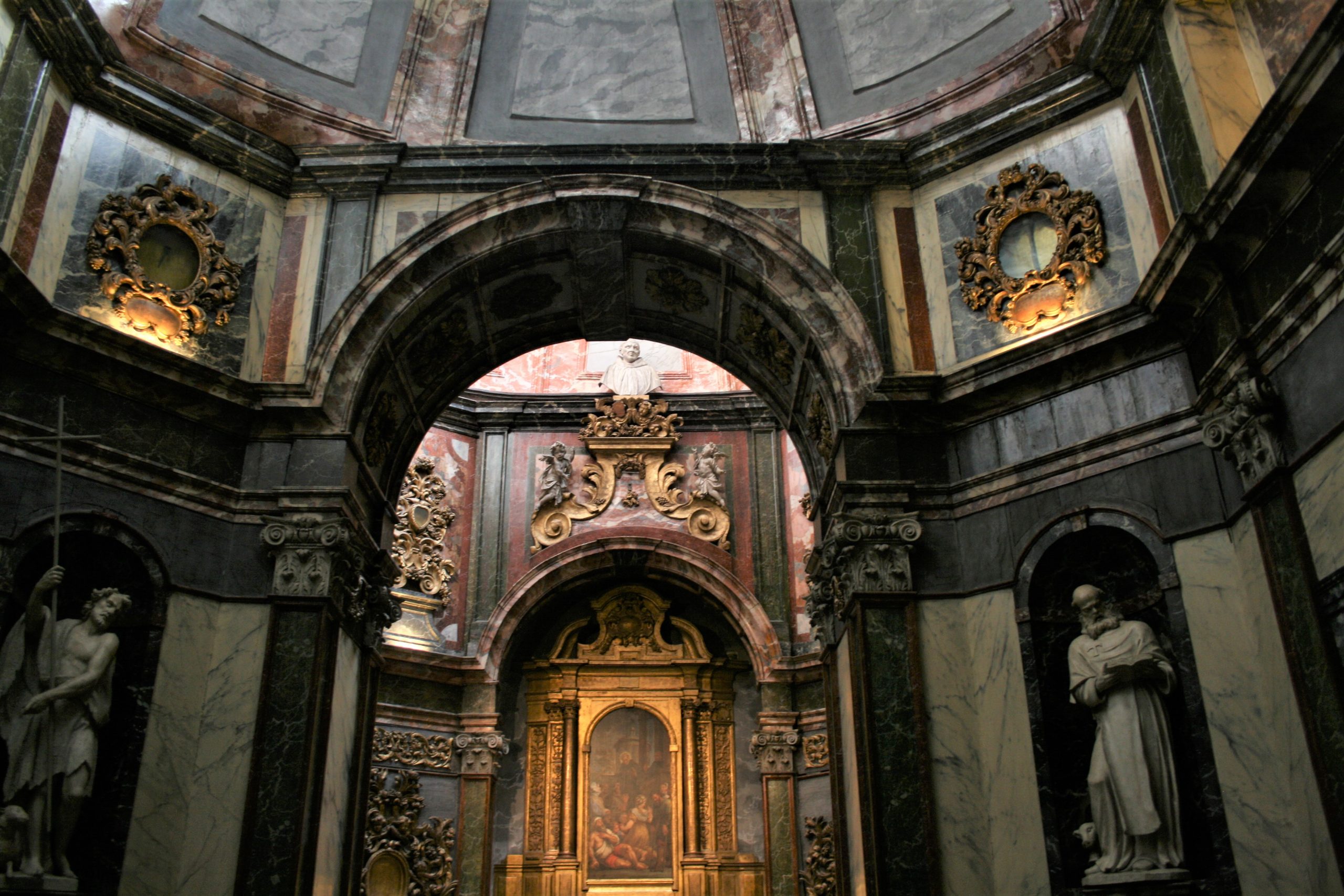 Vue intérieure d'une chapelle éclairée avec des sculptures et des peintures sur les murs.