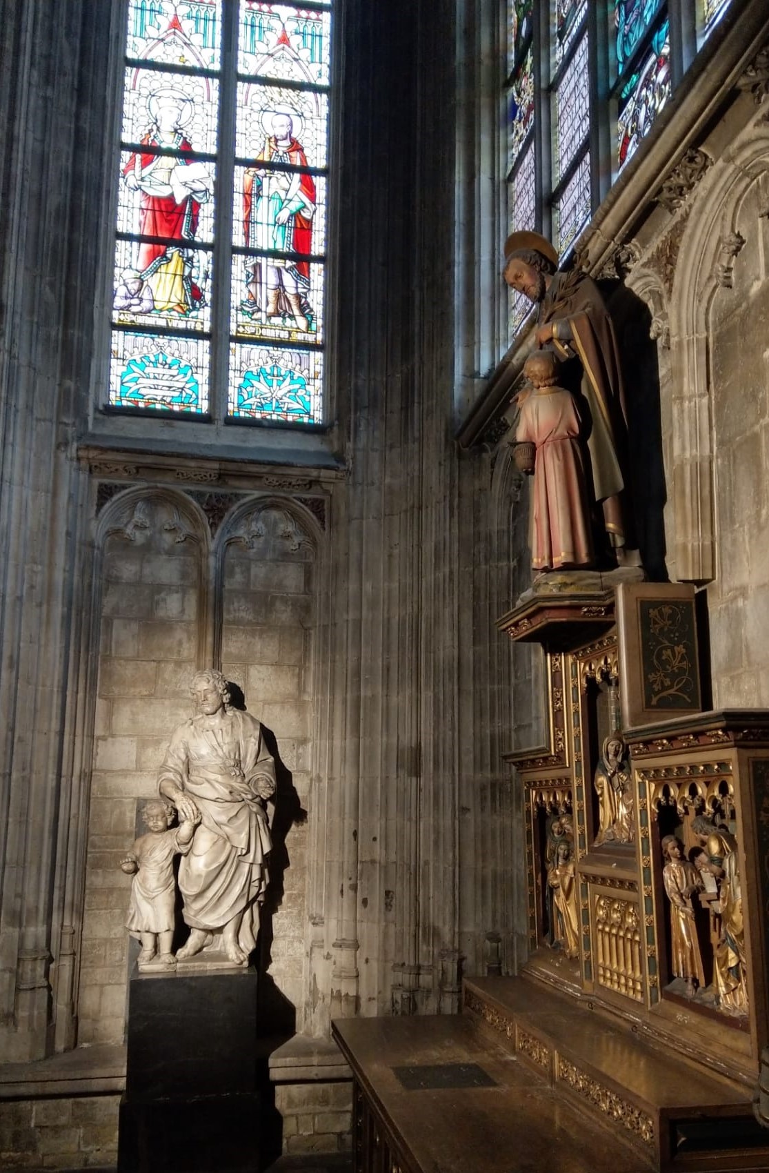 Mise en lumière de la statue de Saint Joseph et l’Enfant Jésus et l’autel attenant avec des vitraux colorés en arrière-plan.