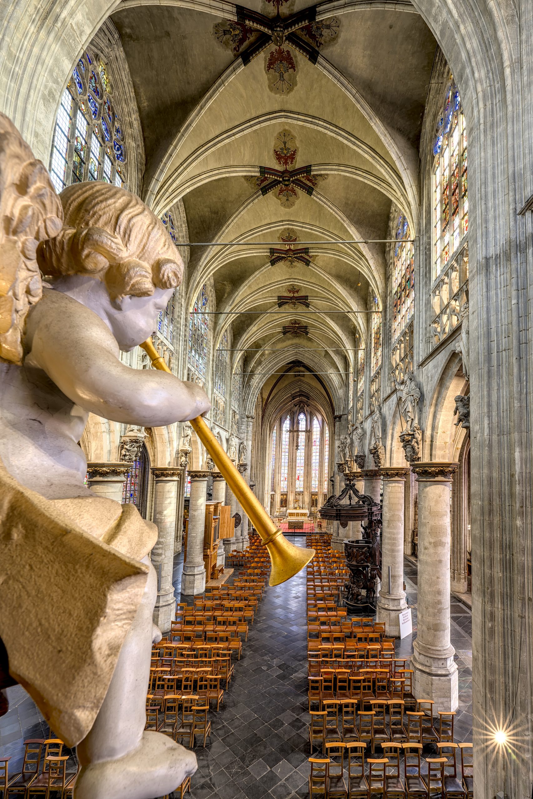 Vue intérieure de l'église Notre-Dame au Sablon avec un angelot tenant une trompette au premier plan et des rangées de chaises en arrière-plan.